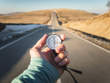 image of person holding compass out in front of them with long road into the desert in front of them