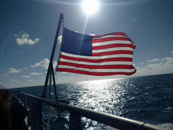 American flag flying on back of a boat with he sun in the background