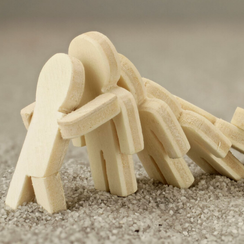 small wood figurines falling like dominoes with the one on the end bracing to stop the next from falling