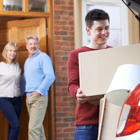 image of parents in doorway of home watching their son loading his vehicle with boxes