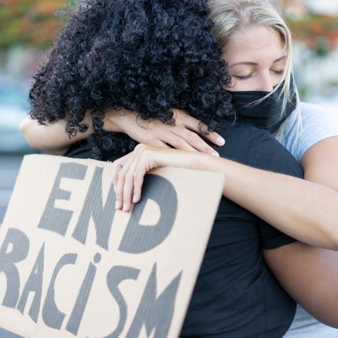 black and white woman hugging. white women holding a sign that says "end racism"