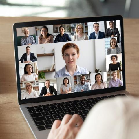 Back view of female employee talk on video call on laptop with diverse colleagues, have group web conference or meeting, woman worker engaged in webcam conversation with coworkers from home