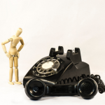 Wood toy human model looking at rotary phone off the hook