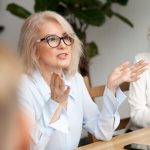 image of woman with elbows on conference table explaining something to others
