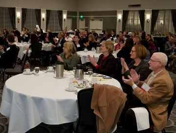 image of a dozen luncheon tables with attendees clapping