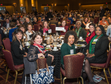 sponsors posing for photo at their table with room of other attendees in the background