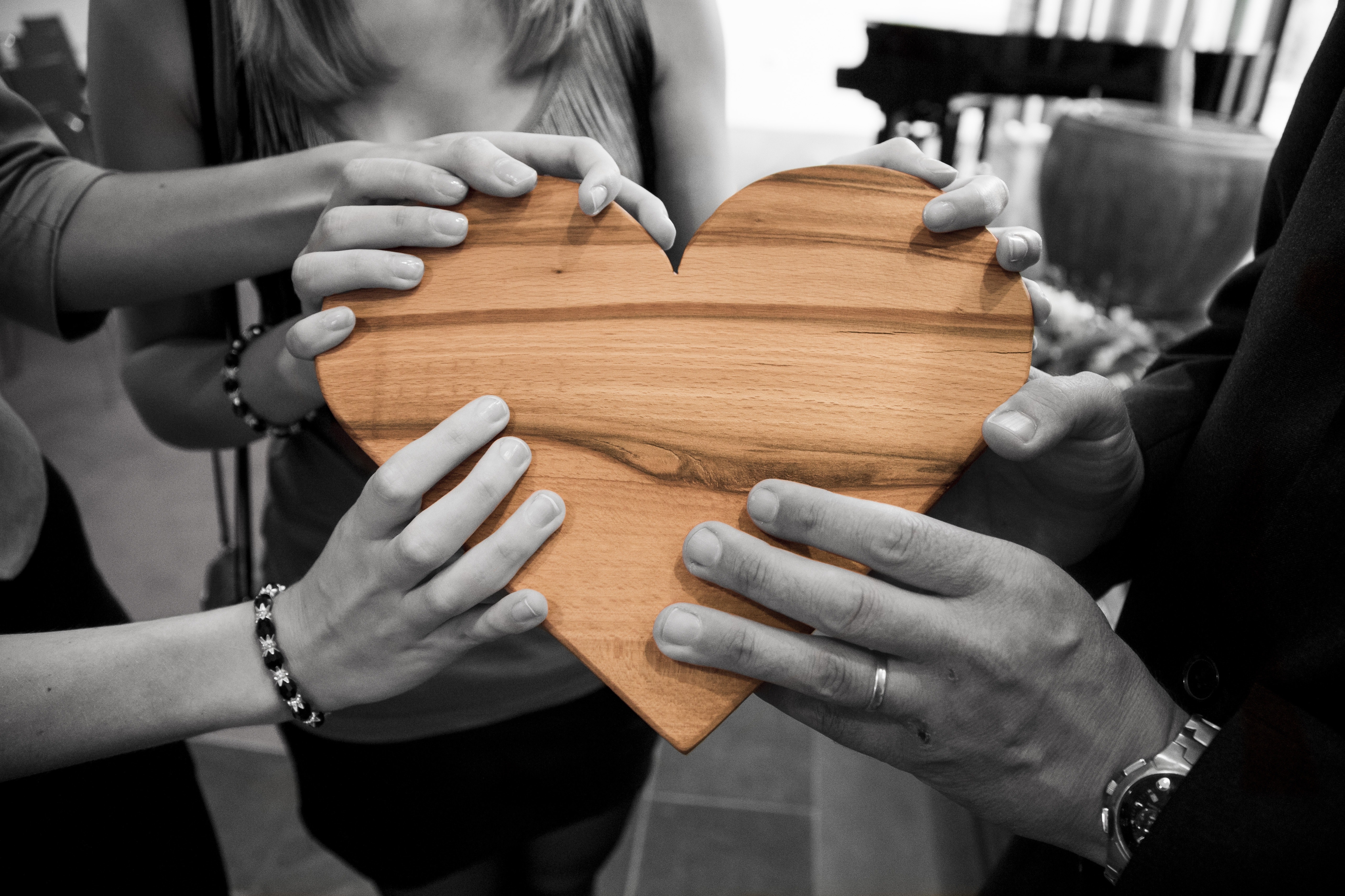 image of several people's hands holding a heart shaped piece of wood