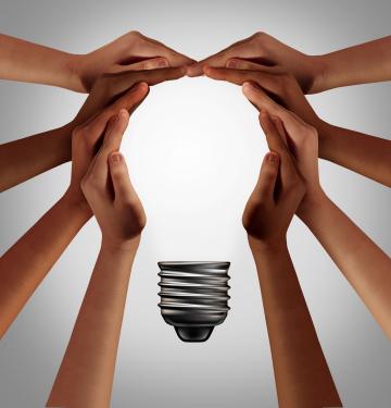 People thinking together as a diverse group coming together joining hands into the shape of an inspirational light bulb as a community support metaphor with 3D elements.