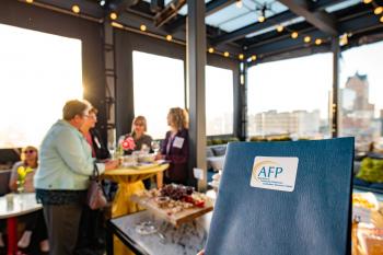 AFP members visiting over wine at a happy hour event. Folder with AFP sticker in the foreground.