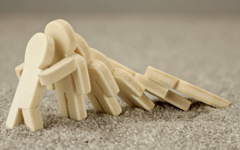 small wood figurines falling like dominoes with the one on the end bracing to stop the next from falling