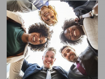 Group of five people in a circle with arms around each other looking downward toward the camera