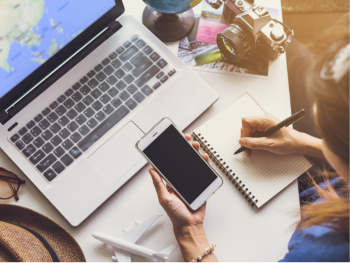 Woman at desk with laptop smartphone, tablet and pen planning a trip