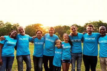 Group of people all various ages and ethnicities with arms around each other. Each wearing a blue "volunteer" shirt.