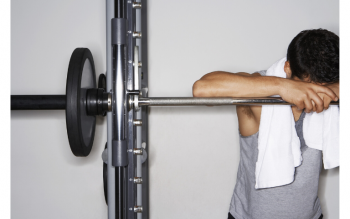 weight lifter with head down on barbell and towel around his neck taking a break