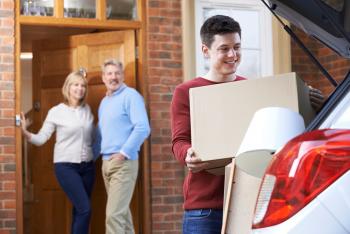 image of parents in doorway of home watching their son loading his vehicle with boxes