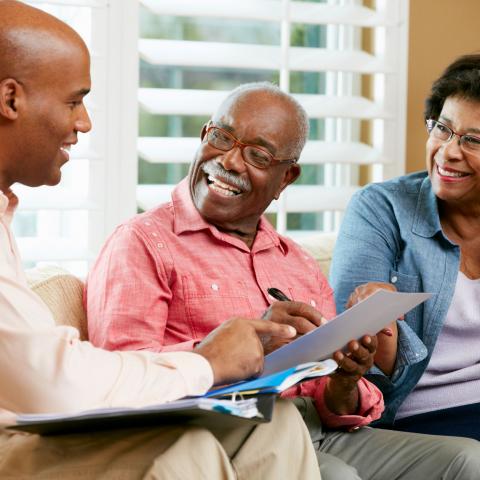 Smiling middle aged black man speaking with smiling older black couple while they sign documents.