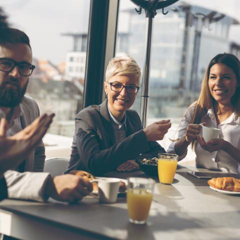 four professionals talking at a table with muffins and orange juice