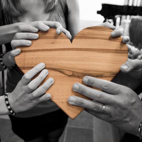 Four sets of hands holding a wood carved heart