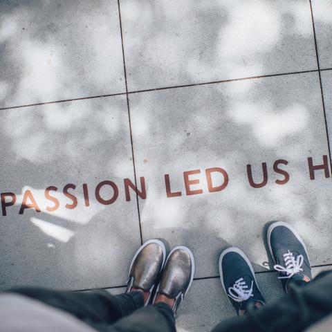 sidewalk with statement "passion led us here" and two pairs of feet with sneakers