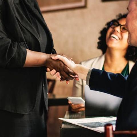 black woman shaking a white man's hand as she approaches the table he and another black woman are sitting at