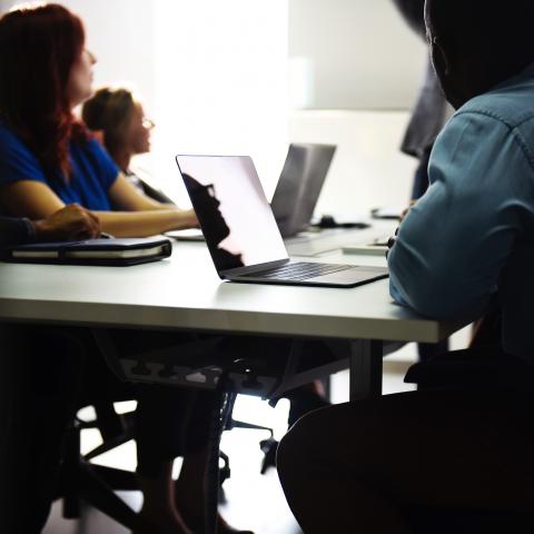 Group of people at a work table looking up toward a video screen