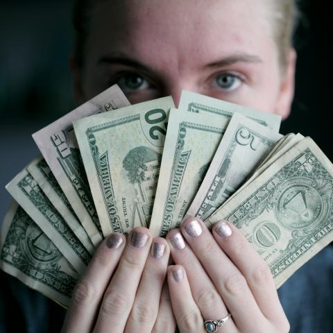 Women holding a fan of cash in front of her covering her face expect for her eyes