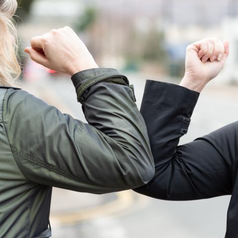 two women bumping elbows in greeting to one another