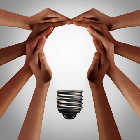 People thinking together as a diverse group coming together joining hands into the shape of an inspirational light bulb as a community support metaphor with 3D elements.