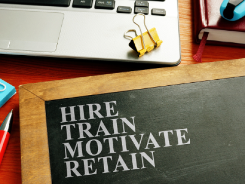 A chalkboard on a desk with the words Hire, Train, Motivate, and Retain