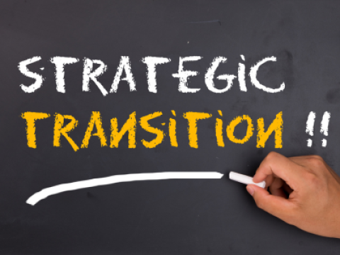 A hand writing "Strategic Transition" on a chalk board