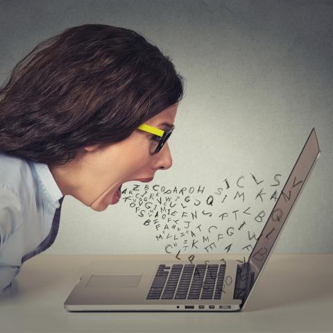 Woman yelling at laptop with small letters come out of her mouth