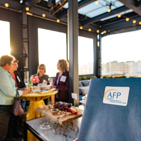 AFP members visiting over wine at a happy hour event. Folder with AFP sticker in the foreground.