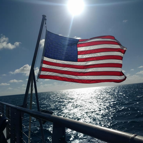 American Flag on back of a boat waving with the sun overhead