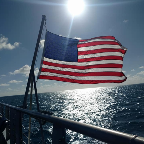 American flag flying on back of a boat with he sun in the background