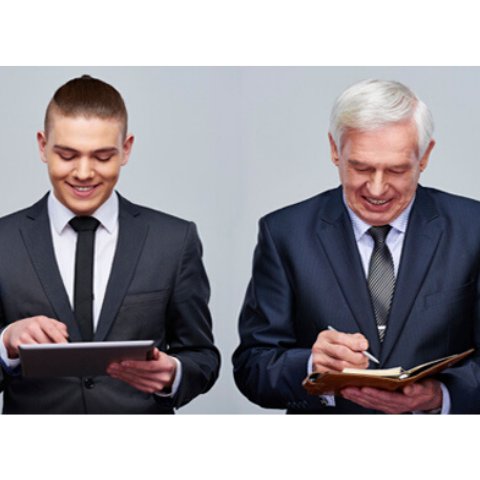 Millennial and gray haired man both in suits standing next to each other working on a tablet and portfolio