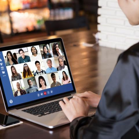 woman at laptop with screen showing fifteen faces of others in the online meeting