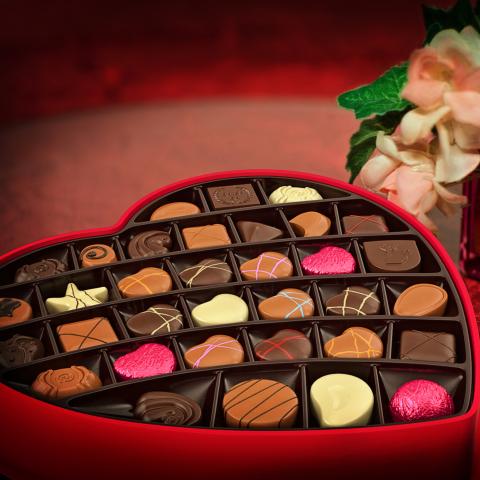 Photo of a box of chocolates next to vase of flowers