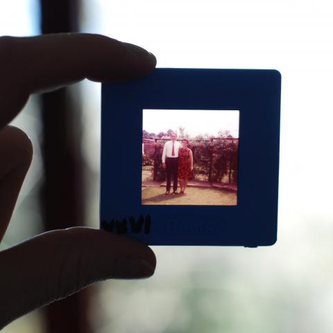 person holding photo slide to the light showing image of older couple in the 1960s