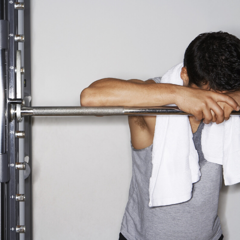 weight lifter with head down on barbell and towel around his neck taking a break