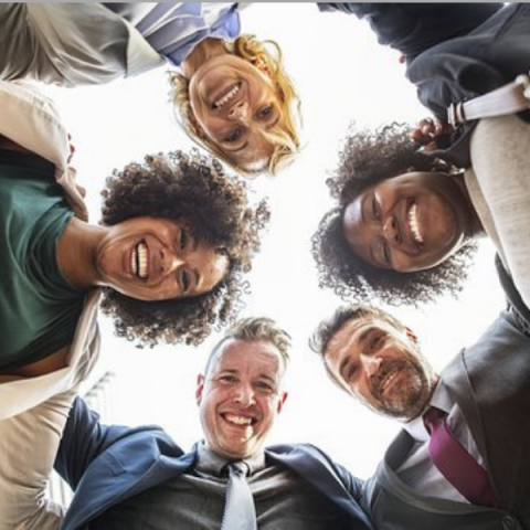 Group of five people in a circle with arms around each other looking downward toward the camera