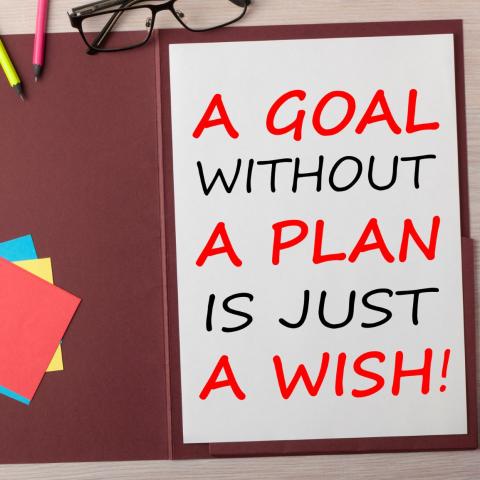 A Goal without a Plan is Just a Wish written in paper sheet on presentation folder and various stationery on wooden table