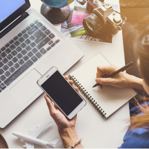 Woman at desk with laptop smartphone, tablet and pen planning a trip