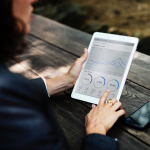 woman sitting on a park bench working on tablet showing graphs and charts