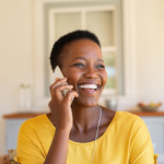black woman smiling while on a cell phone call in her living room