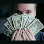 young woman holding a "fan" of cash covering half her face
