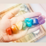 hand holding seven rocks and minerals arranged in the color of the rainbow